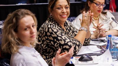 Women sitting at a conference table, smiling and clapping, with papers and water bottles in front of them.