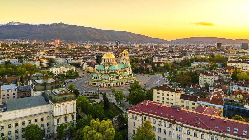 Aerial view of Sofia at sunset, with Alexander Nevsky Cathedral and mountain backdrop.