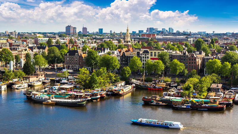 Canal view of a city with boats and green trees under a blue sky with clouds.