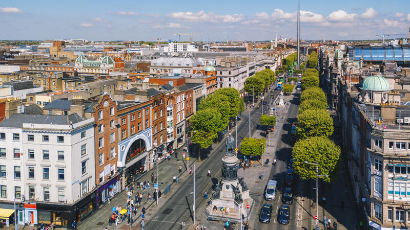 Aerial view of a busy city street lined with trees and buildings, under a clear blue sky.