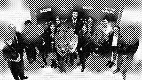 A group of people standing together, smiling, in front of a blue backdrop with text.